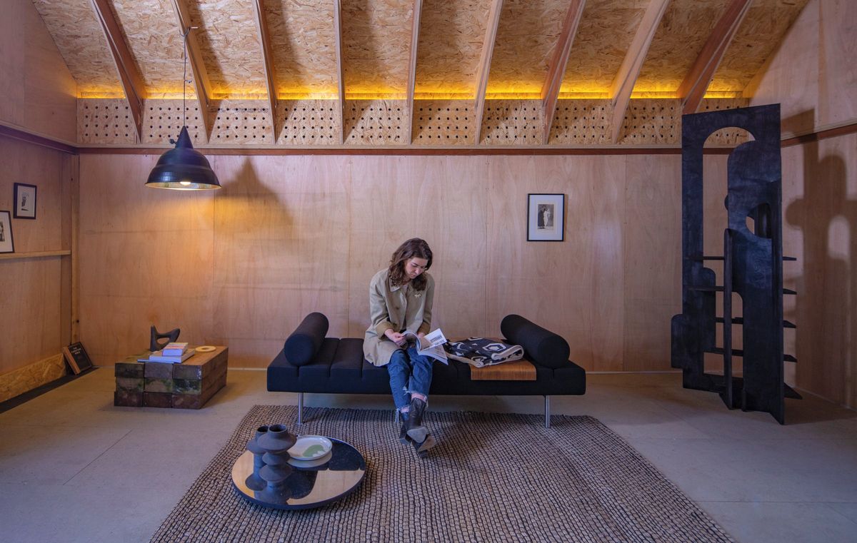 Woman reading on the daybed beneath the lit roof ribs