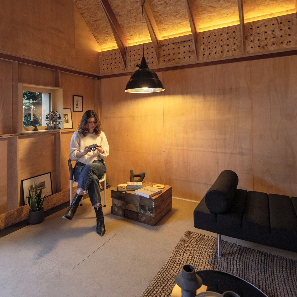 Woman reading in an armchair under the pendant light, wall niches behind