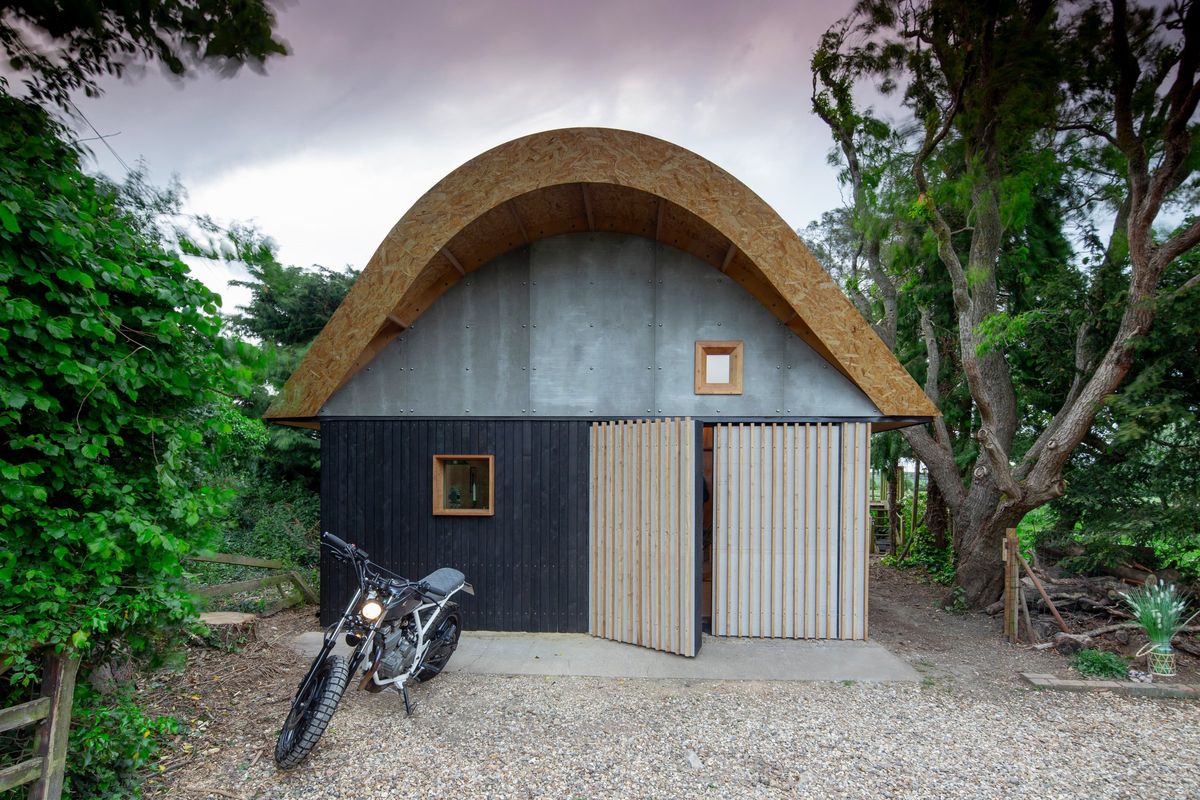 The barn front with its curved roof, doors half open, motorbike outside