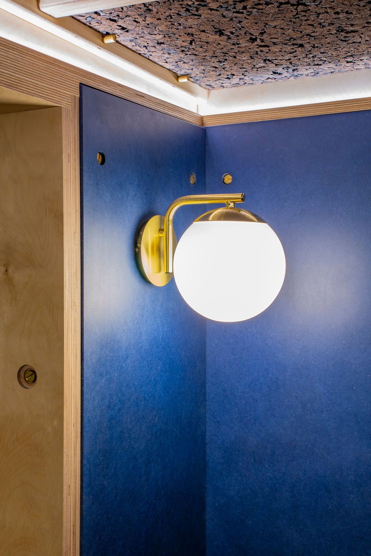 Brass globe wall light on blue panels under the cork ceiling