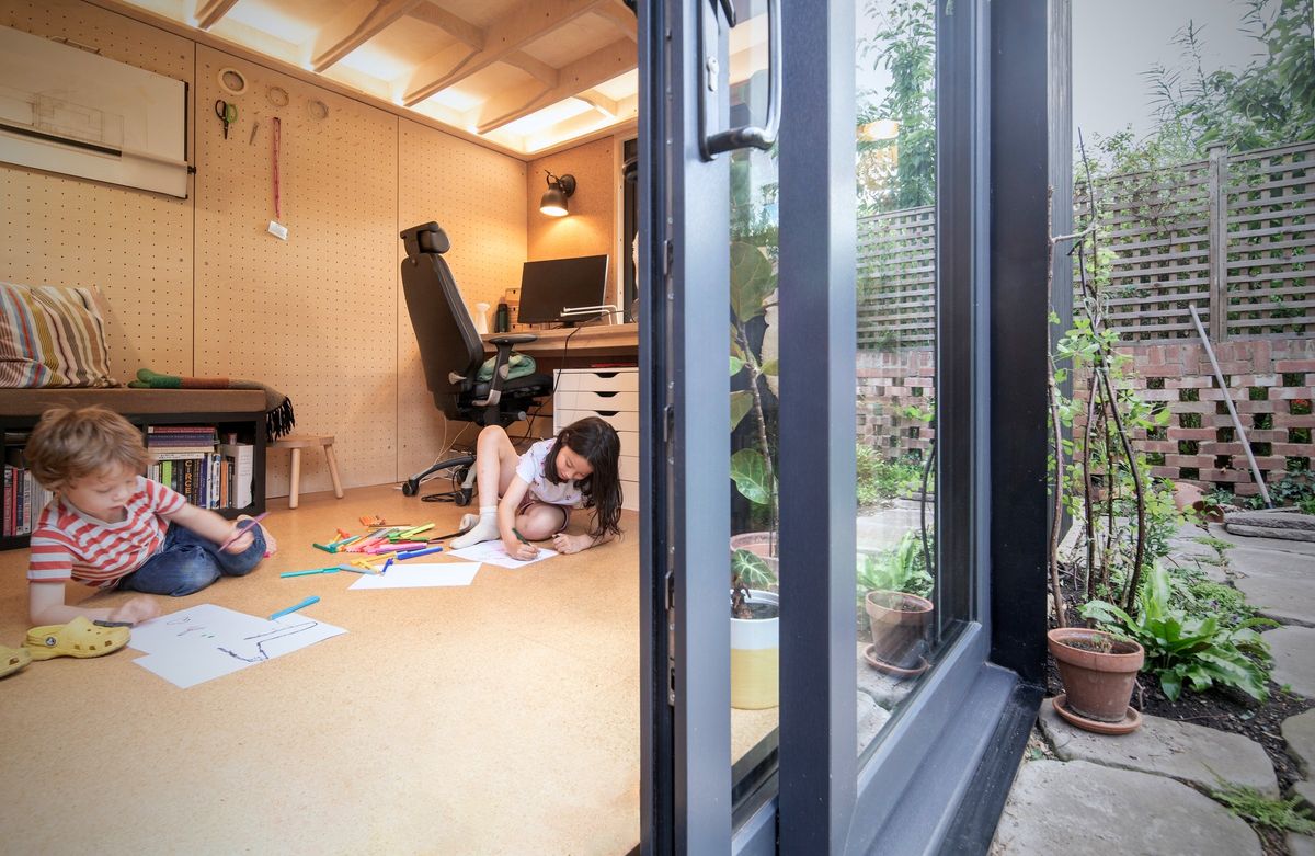 Children drawing on the floor of the garden office, desk and bookshelves behind