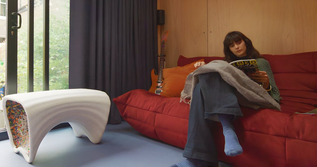 Woman reading on the red sofa in the garden cinema room, curtain and sliding door behind