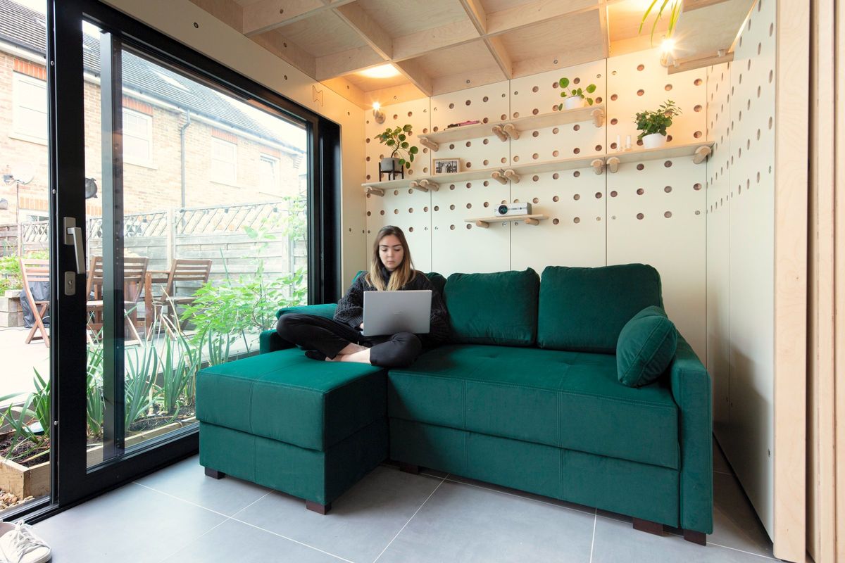 Woman working on a laptop on the green sofa by the glass doors