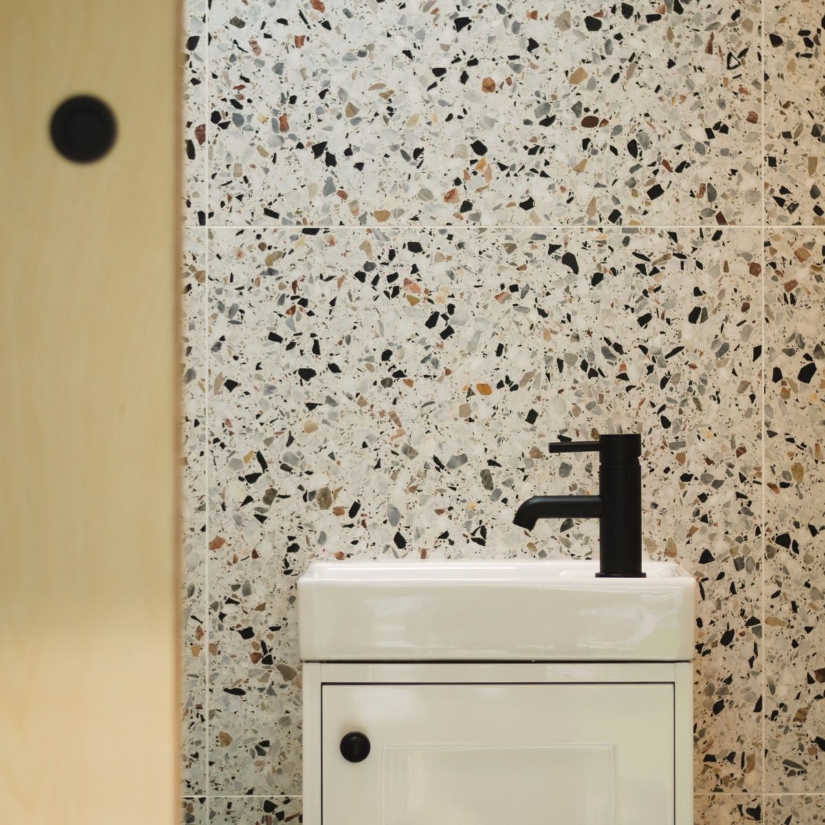 Black tap and white basin against the terrazzo wall
