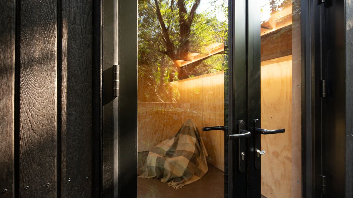 Glazed door against the charred cladding, warm interior beyond