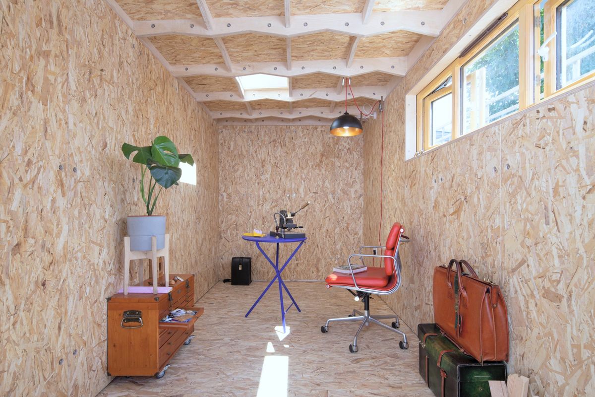 Inside the industrial-style studio: OSB walls, skylight, clerestory windows, desk and red chair