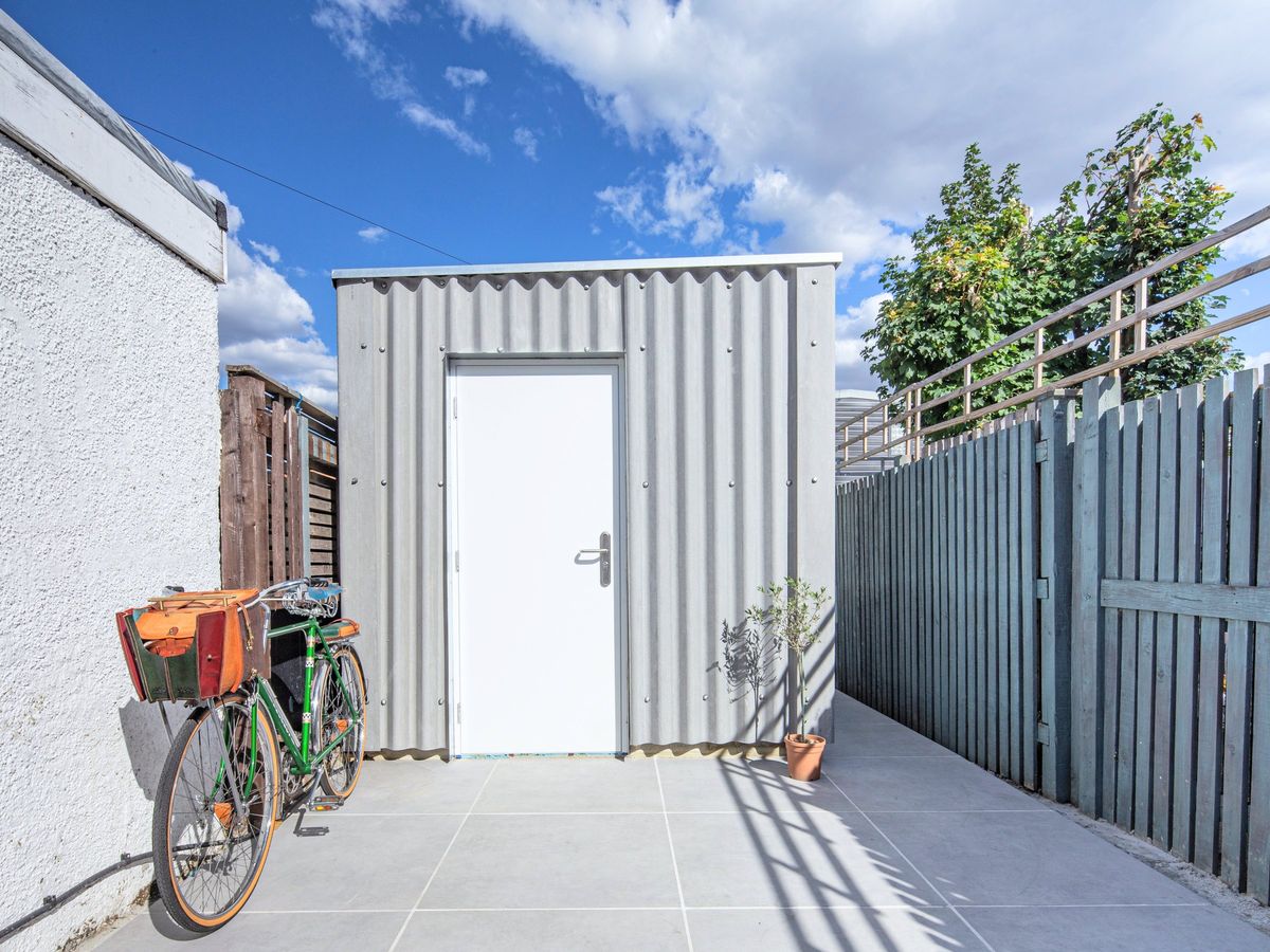 Grey corrugated studio with its door closed, a bicycle beside it
