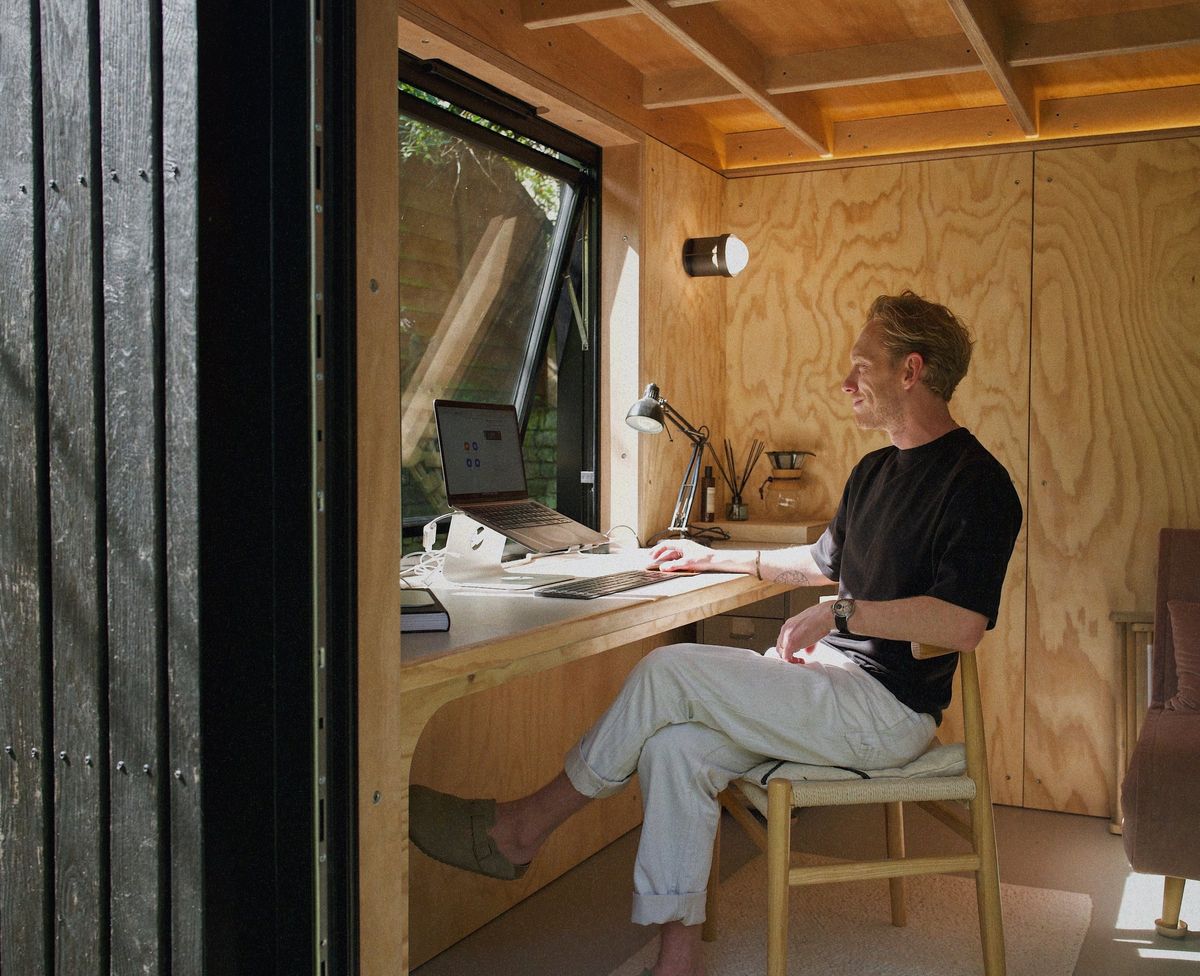 Man working at the curved plywood desk in the garden office, looking out of the window