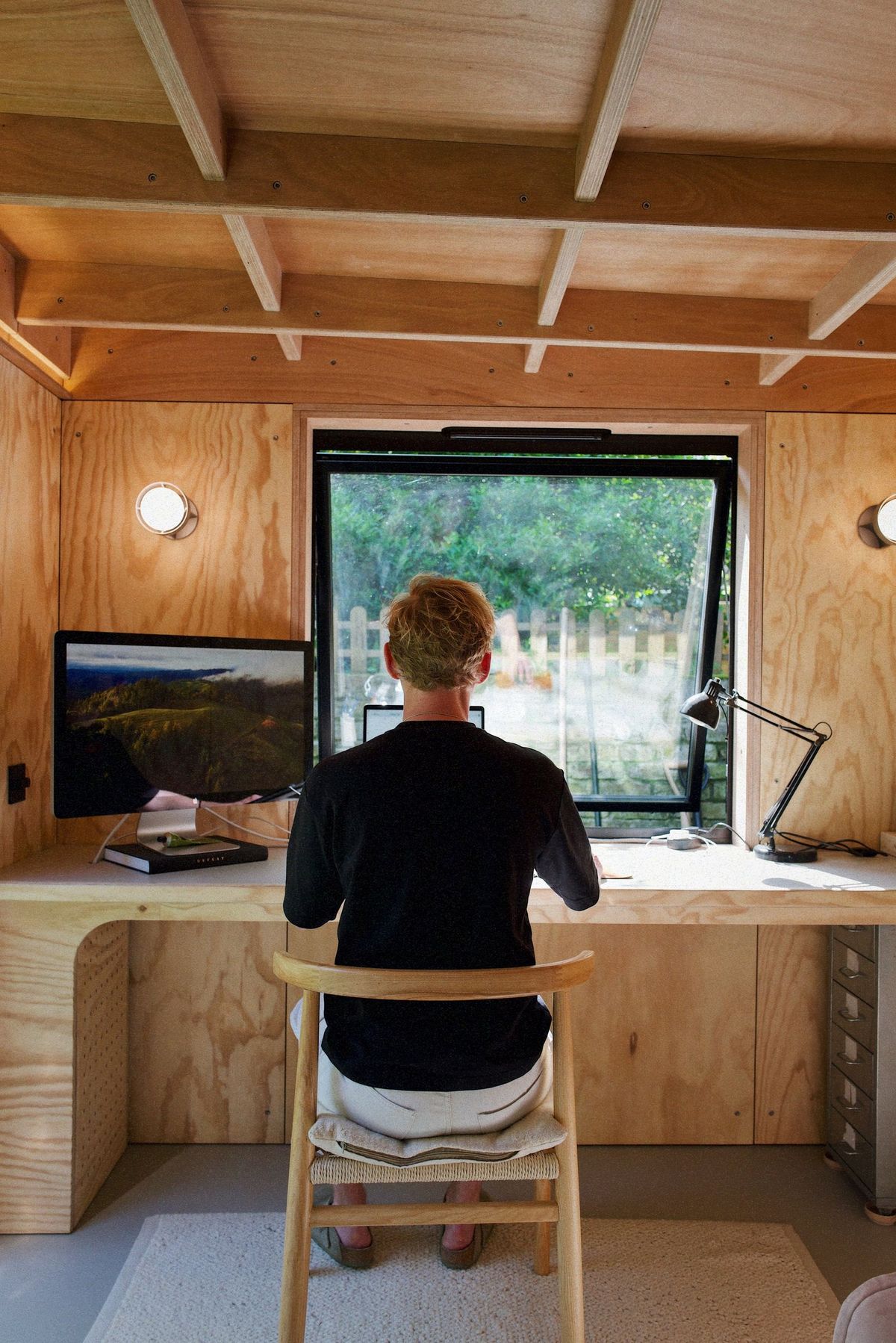 Working at the garden office desk, seen from behind, the window onto the garden ahead