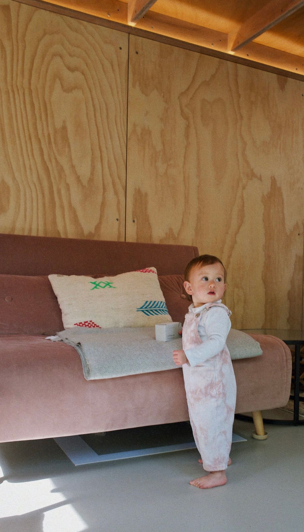 Baby standing by the pink sofa in the garden studio