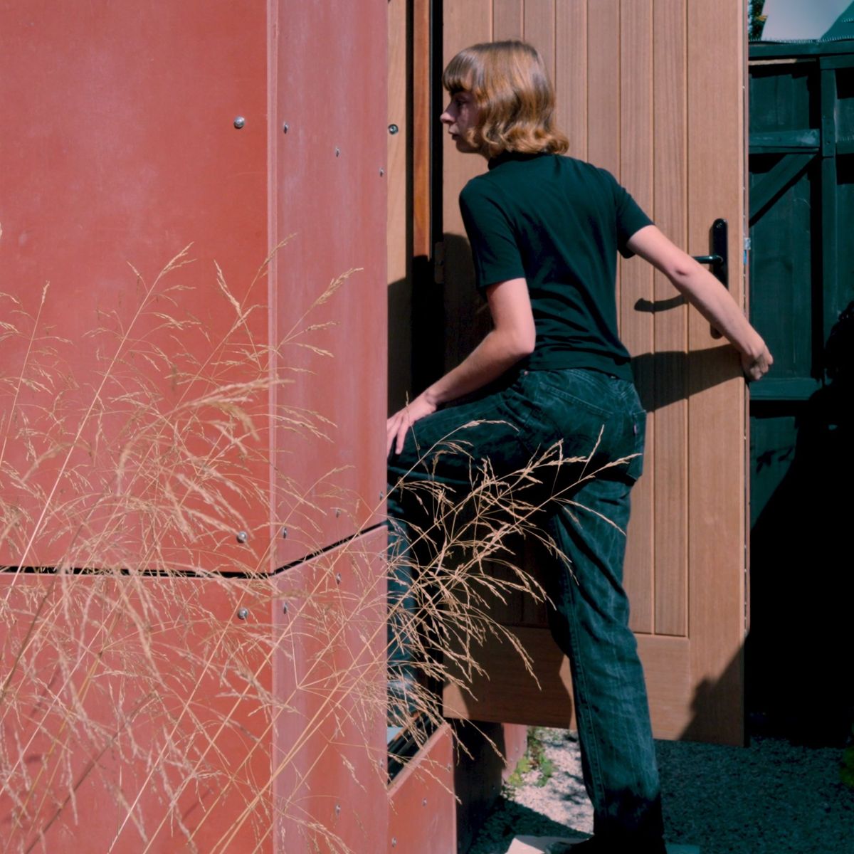 Stepping into the music studio through its door in the red cladding, grasses in front