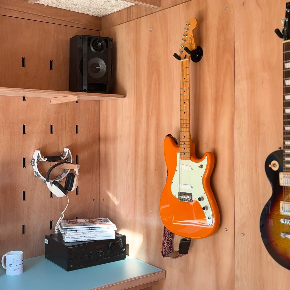 Guitars, headphones and a speaker hung on the plywood peg wall