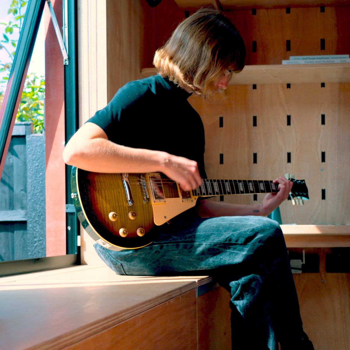 Playing guitar on the window bench, peg wall behind