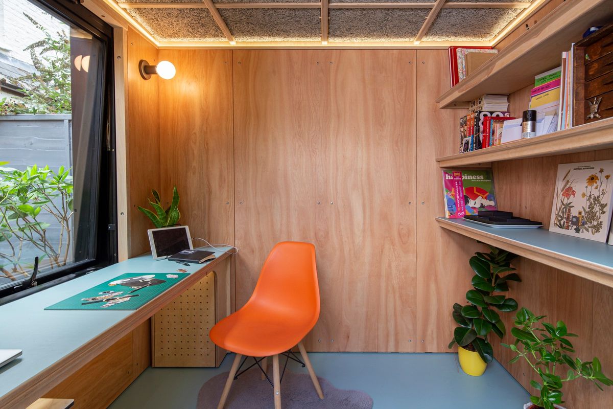 The whole pod: desk under the window, shelves and orange chair