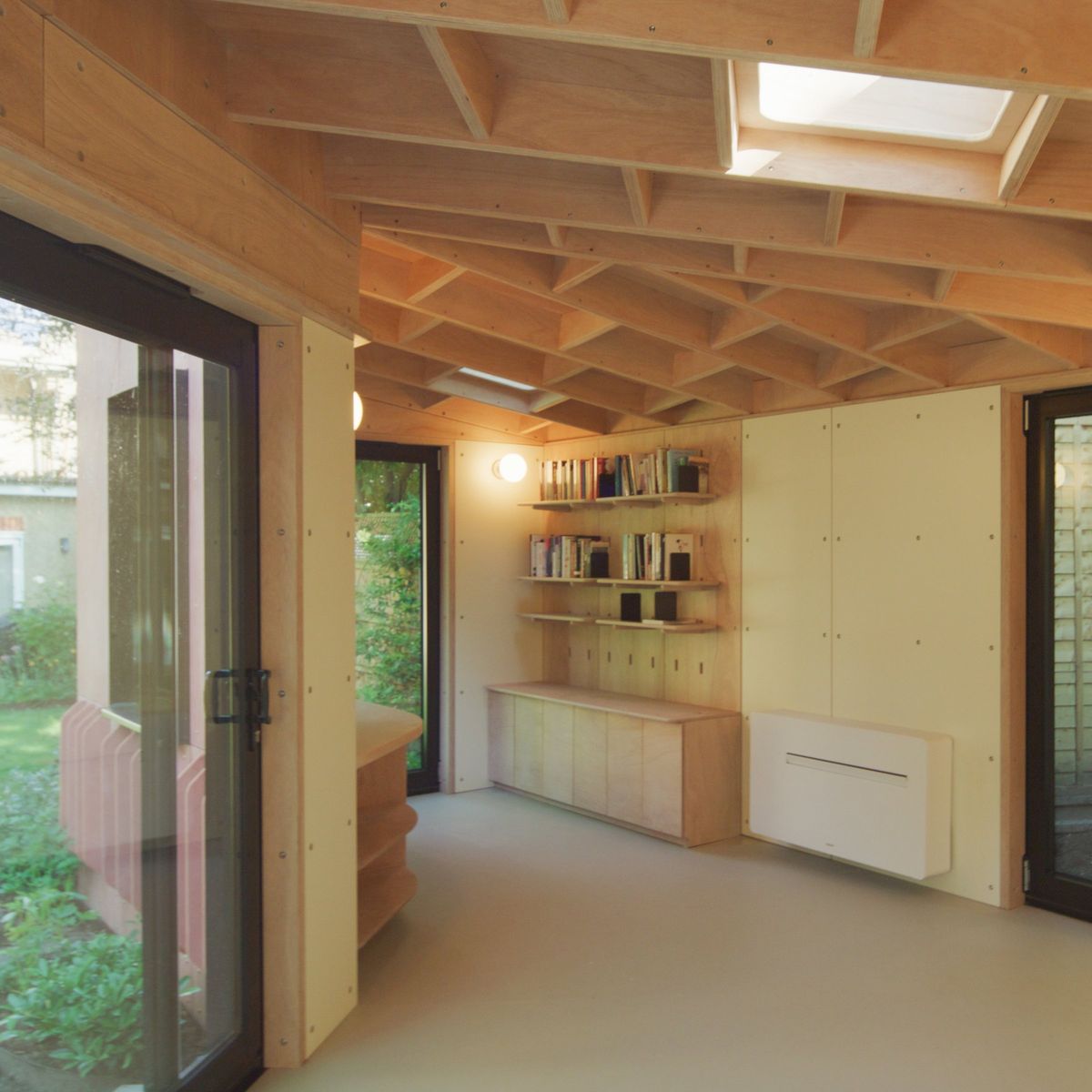 Inside the red garden studio: ribbed plywood ceiling, skylight, bookshelves and a storage wall