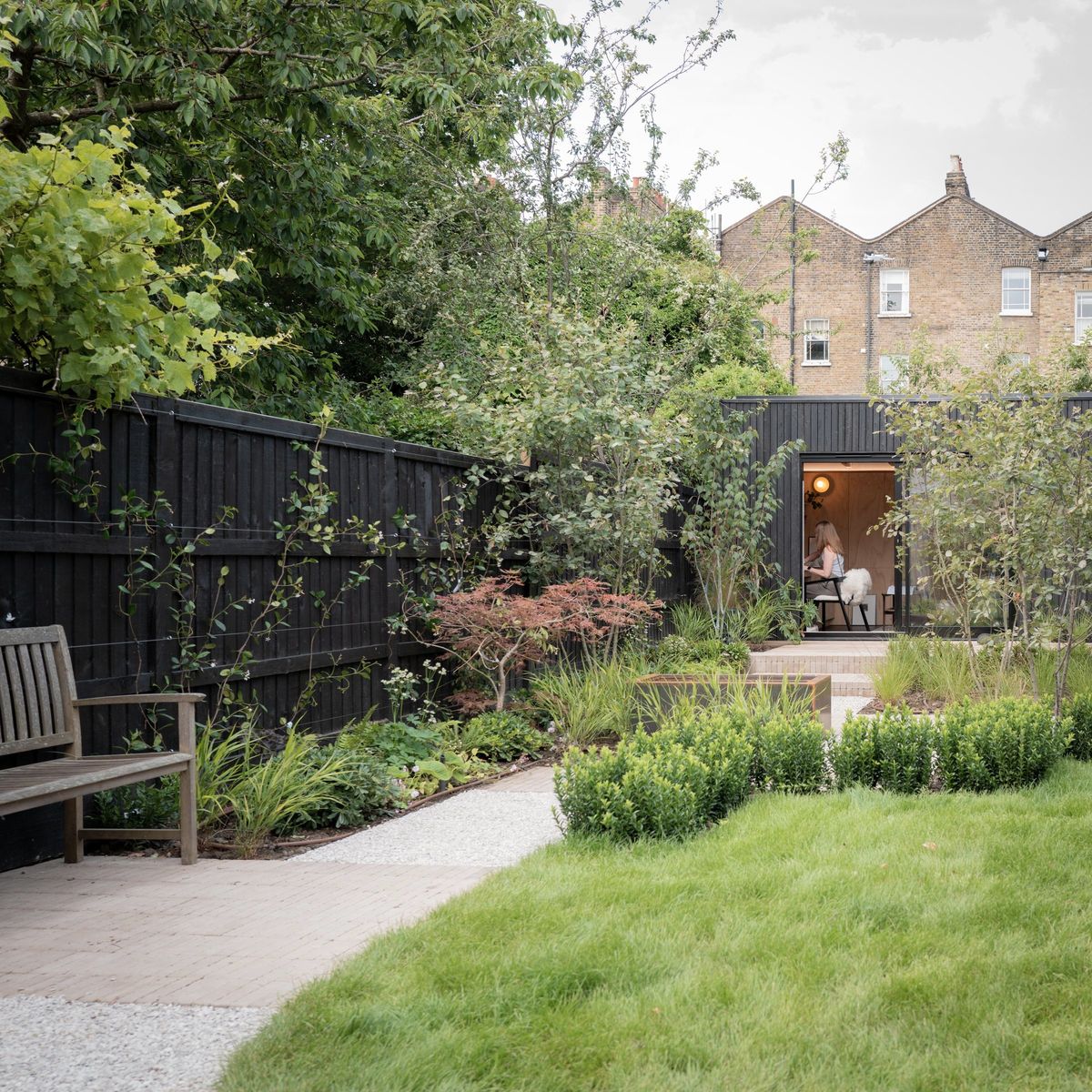 Path through a planted Peckham garden to a charred-timber L-shaped garden room at the far end
