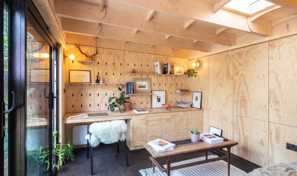 Garden studio interior with a skylight, exposed plywood ceiling joists and a full-width desk