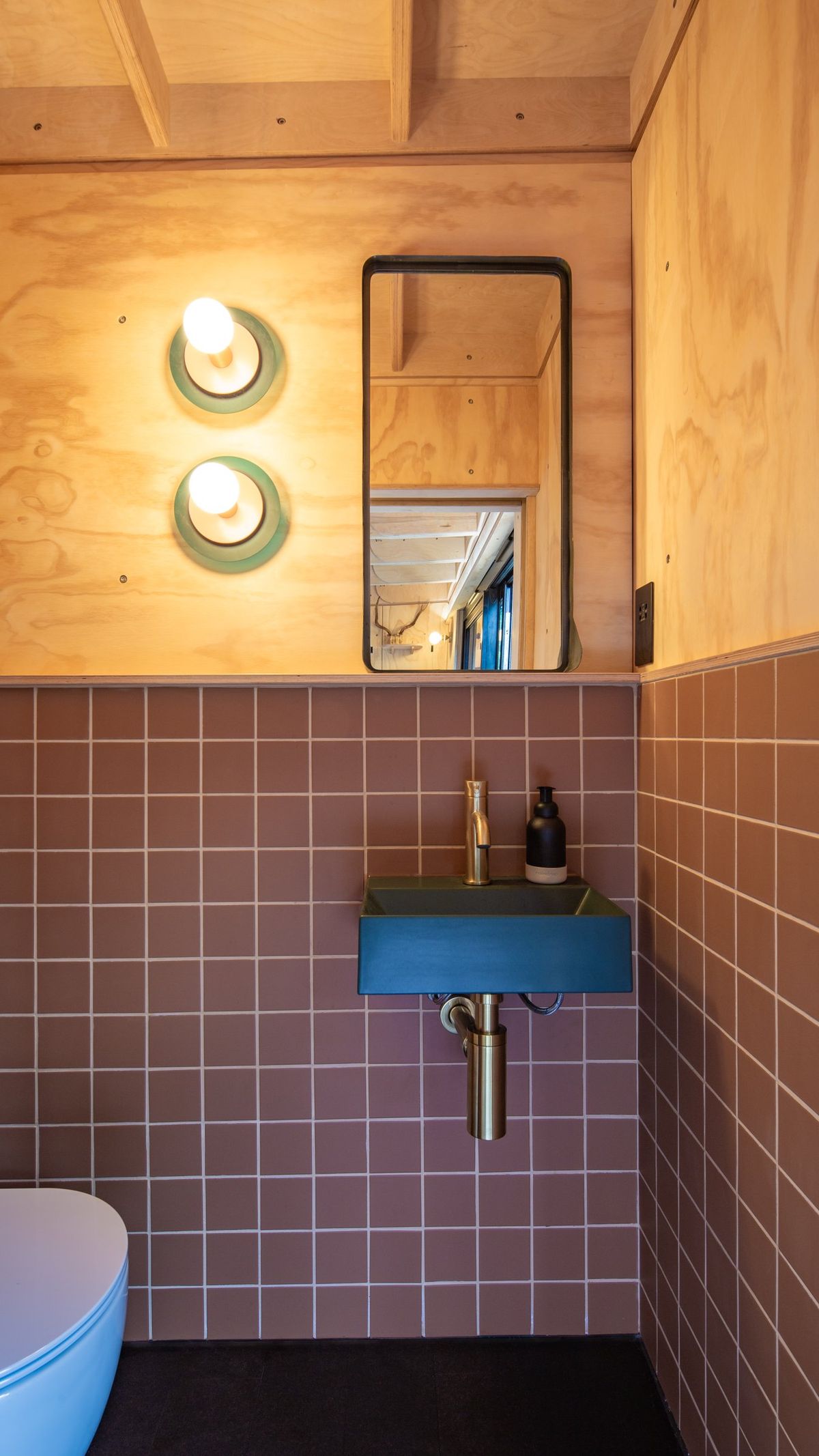 Garden studio WC with terracotta tiles, a teal basin, round wall lights and a wall-hung toilet
