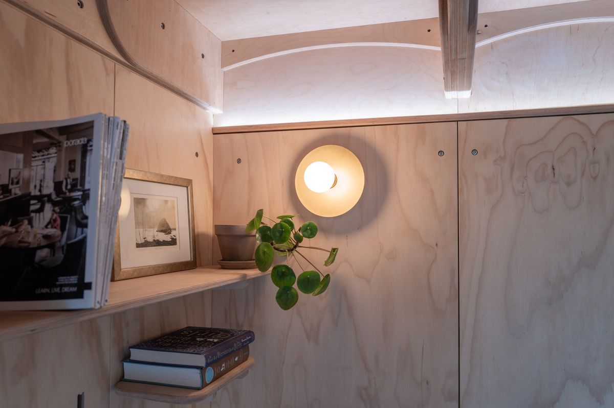 Plywood wall with a round wall light, a shelf of books and a framed print