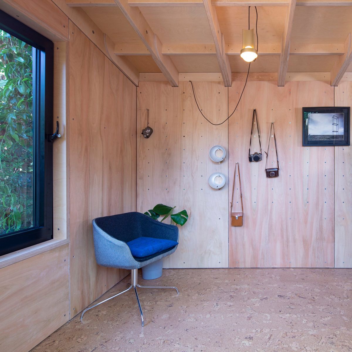 Blue armchair beside the window, cameras hung on the plywood wall