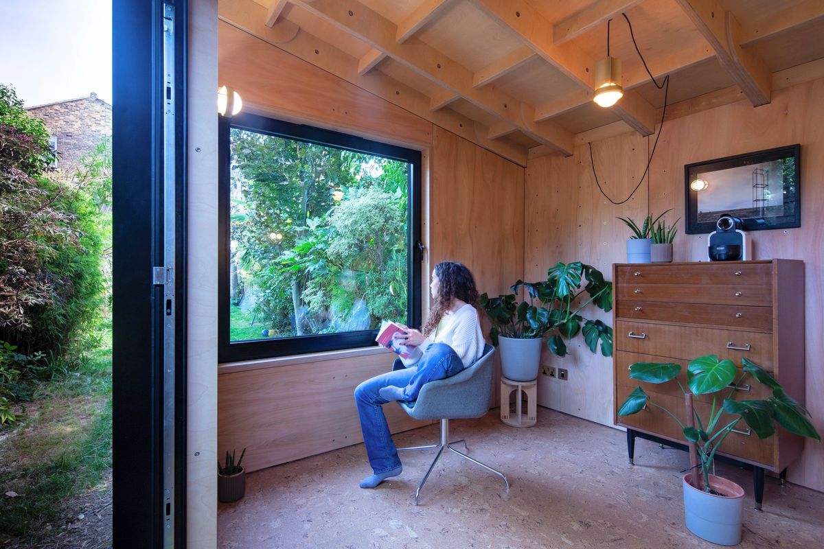 Woman reading in the blue armchair by the corner window and open door