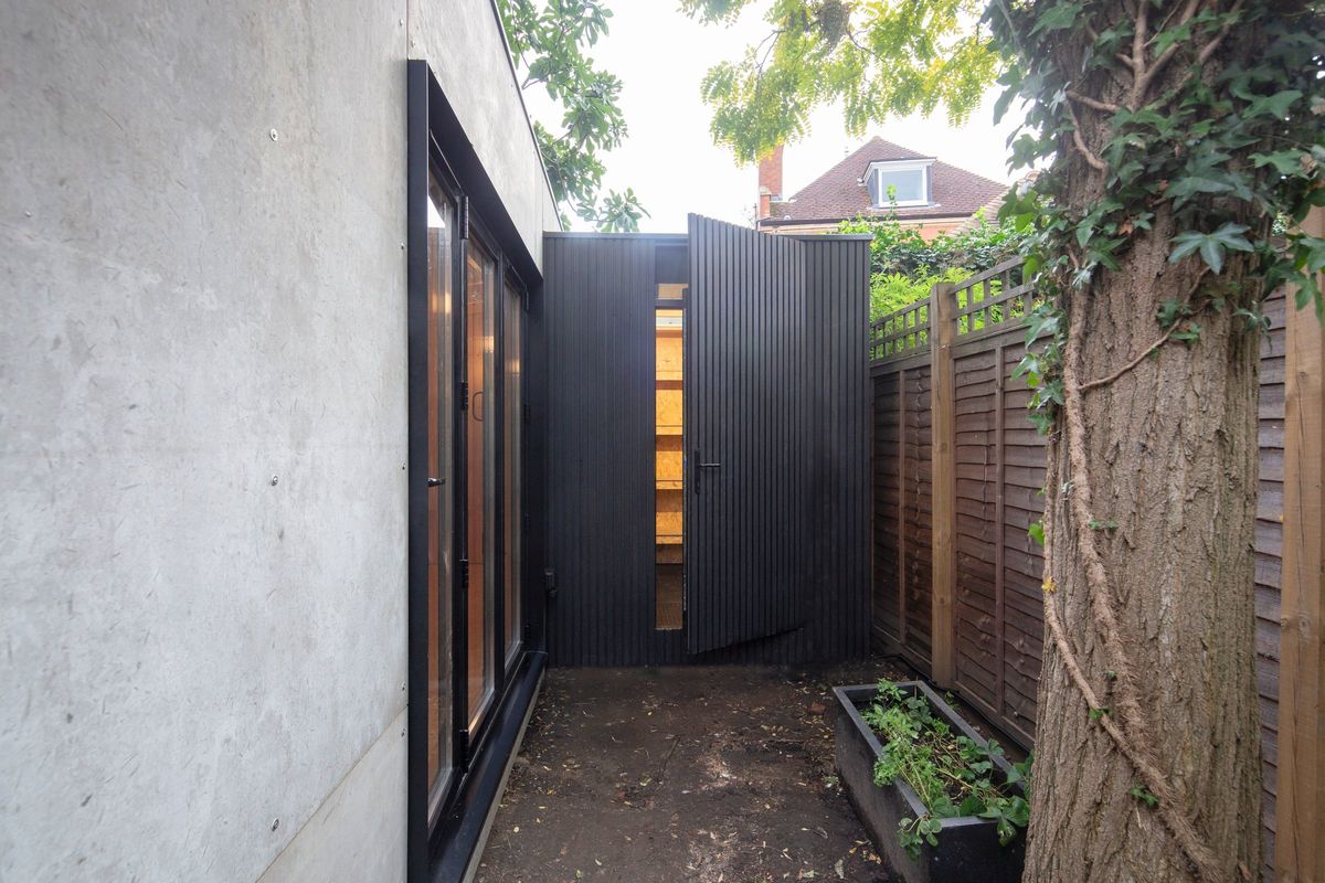 Side path to the clad storage room, its door open on the shelves