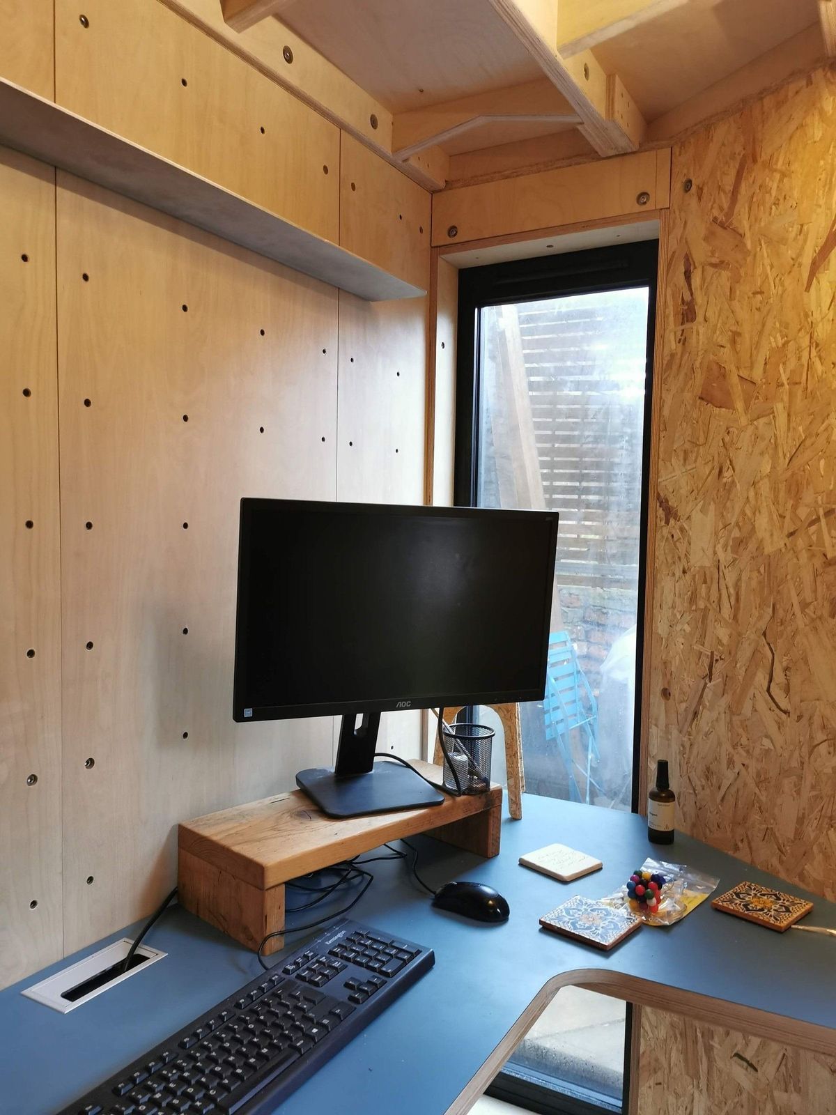 Corner desk with a monitor under the slim window, peg wall beside