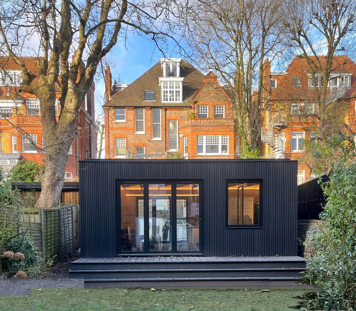 Dark grey clad garden room in Swiss Cottage with full-height glazing and steps leading to bi-fold doors